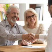 An elderly man and woman shaking hands with an insurance advisor
